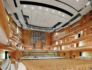 The hall has three balconies, and audience seating wraps around the stage. The top of the room is crowned by multi-part suspended motorized sound reflectors. Photo © Tom Arban