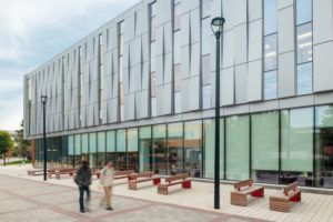 The street-style lampposts and casual seating with bike parking create a safe and informal environment for students to socialise together beneath the shelter of an overhanging roof.