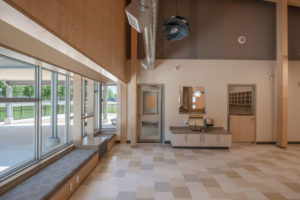 The common area has an alcove by big windows to let in natural light. The cubbies area is evident behind the door to the right of the washing area.