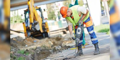 Builder worker with pneumatic hammer drill equipment breaking asphalt at road construction site