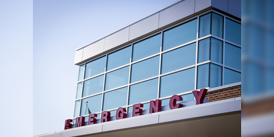 Emergency room entrance with red block letters on the metal awning of a hospital building, blue tone filter.