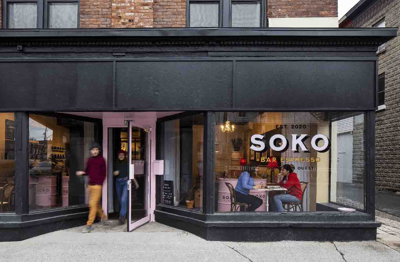 A café named Soko Bar Espresso, with customers inside and two people exiting the pink door.