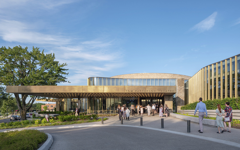 The Tom Patterson Theatre features a modern entrance with golden accents, surrounded by lush greenery and a clear blue sky.