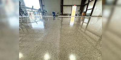 Shiny, polished concrete floor inside a spacious industrial building, with chairs and tools visible in the background.