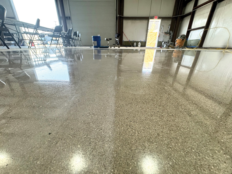 Shiny, polished concrete floor inside a spacious industrial building, with chairs and tools visible in the background.