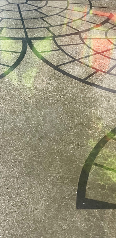Close-up of a textured floor with a dark web-like design, reflecting subtle hints of green and orange light.