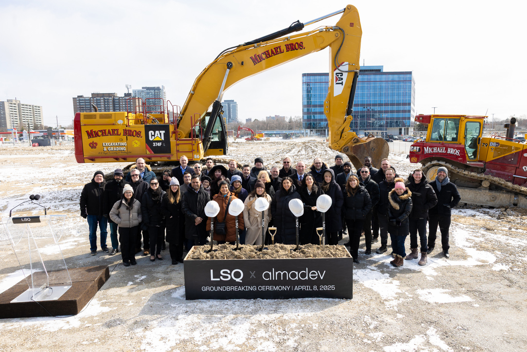 A group of people gathers for the LSQ x Almadev groundbreaking ceremony in front of construction equipment on a snowy Toronto site.