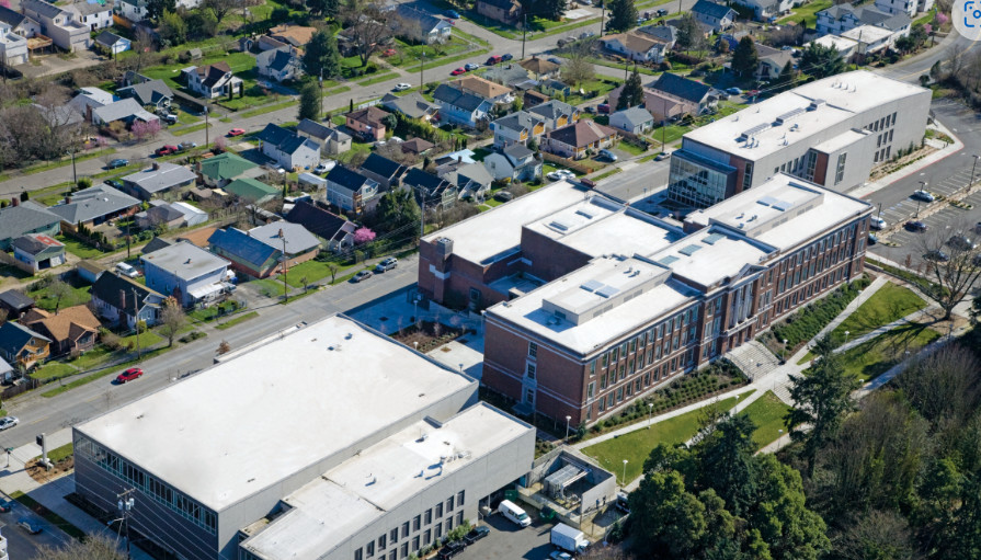 Aerial view of modern buildings adjacent to a residential neighborhood, featuring green spaces and tree-lined streets.