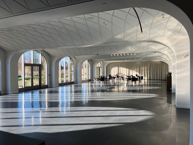 Bright, modern event space featuring arched windows, polished floors, and a set dining area, with soft shadows and natural light.
