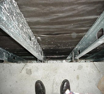 Top-down view of a dark, narrow space with metal supports and a concrete floor, featuring a person's black boots at the edge.