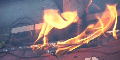 Flames flicker and dance around a metallic surface, with vivid orange and yellow hues against a dark background.
