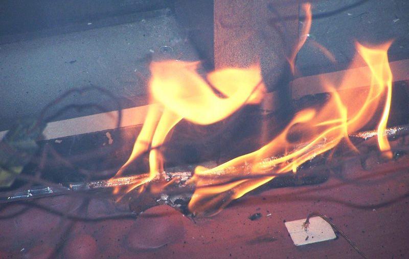 Flames flicker and dance around a metallic surface, with vivid orange and yellow hues against a dark background.