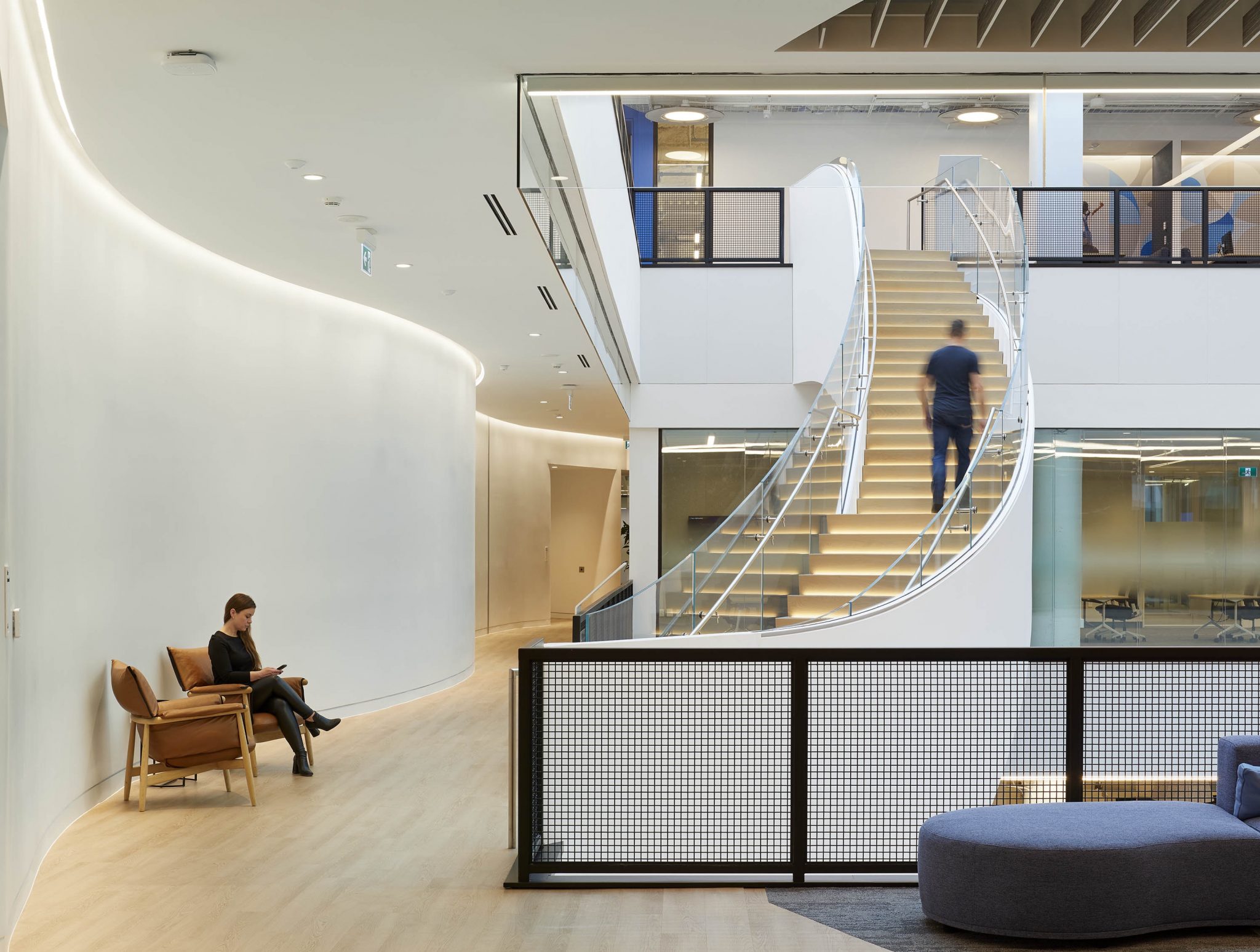 A modern office interior featuring a curved white wall, a stylish staircase, and contemporary furniture placed in a spacious, bright environment.
