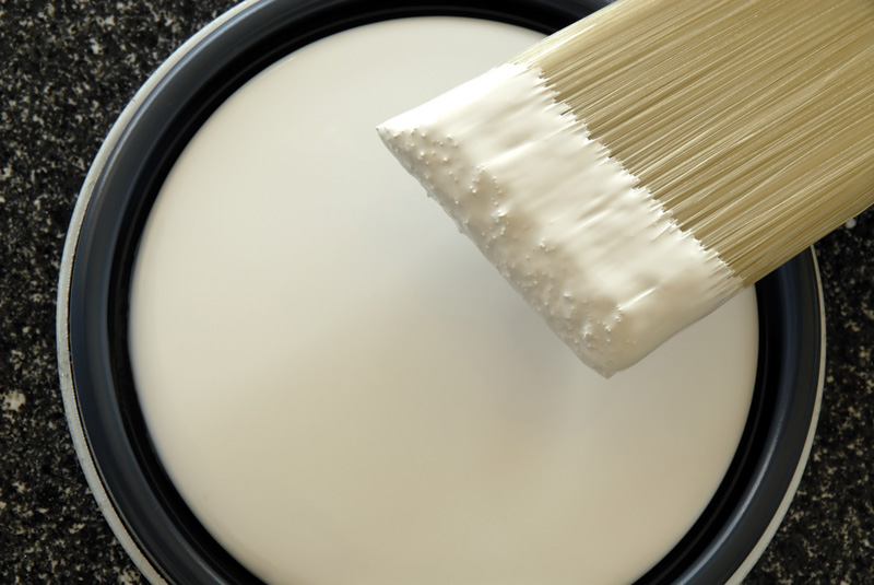 A paintbrush dipped in smooth, white paint above a can, set against a dark textured surface.