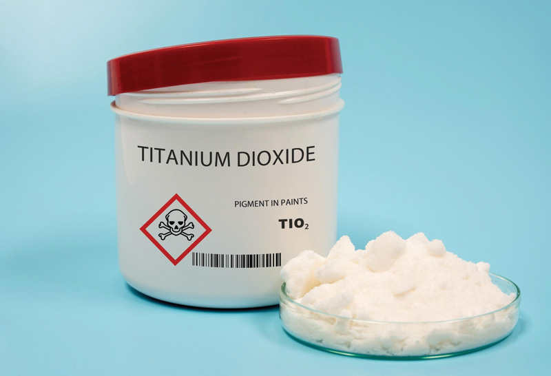 A container labeled "Titanium Dioxide," with a warning symbol, alongside a dish of the white powder.