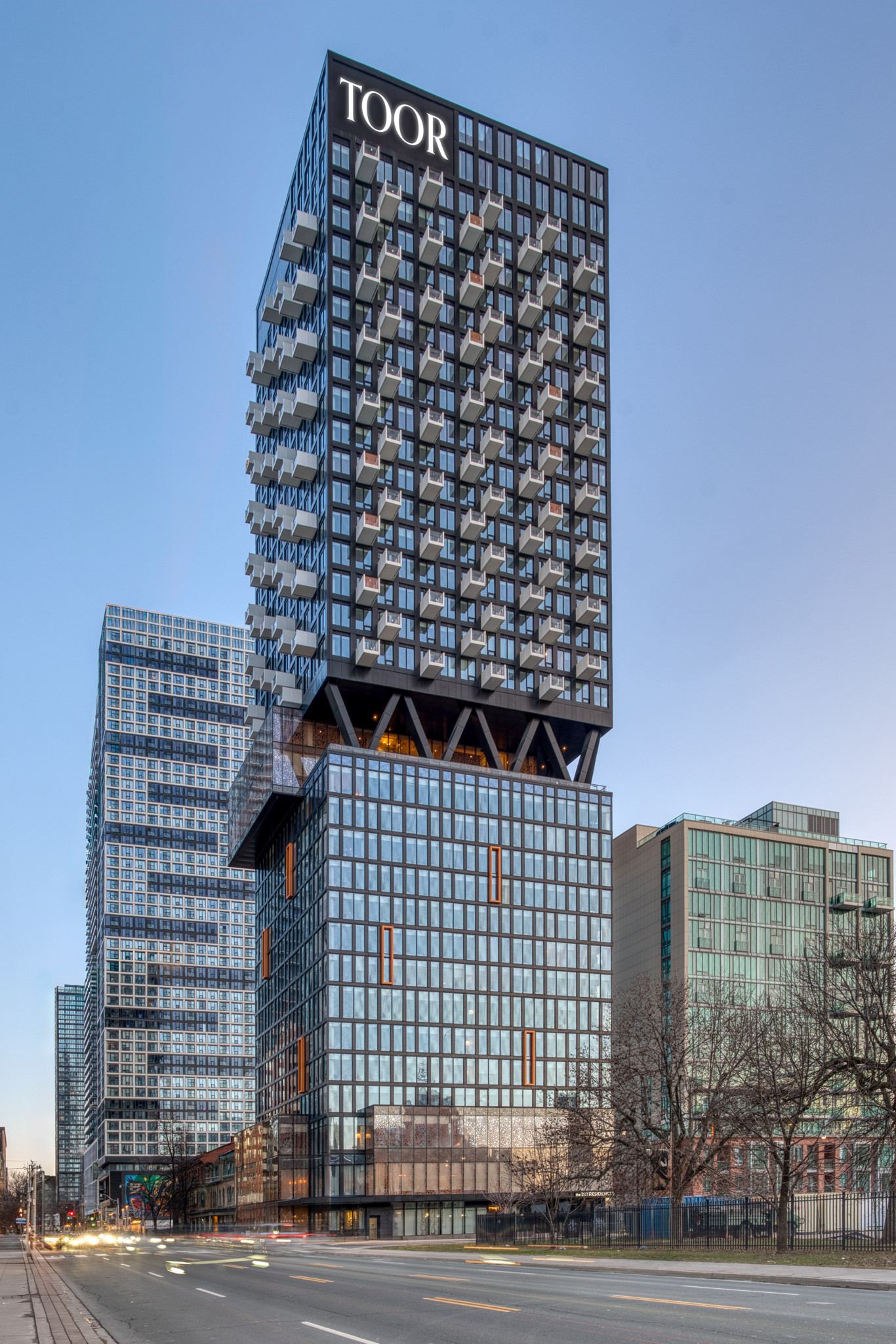 TOOR tower features a cantilevered design with bold balconies, glass cladding, and striking structural supports on a busy city street.