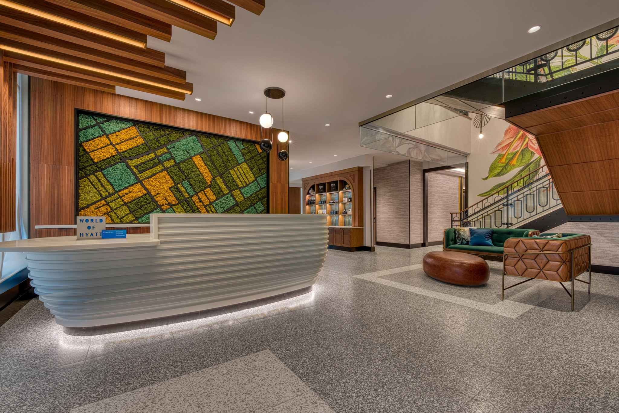 Hotel lobby with terrazzo flooring, a ribbed white reception desk, colorful mosaic wall art, modern seating, and warm wood ceiling accents.