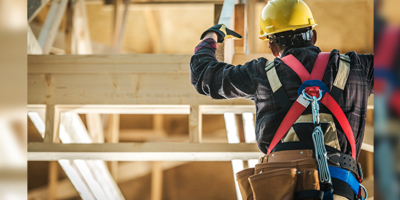 A construction worker in a yellow hard hat and harness climbs wooden beams, focusing on safety and the task at hand.