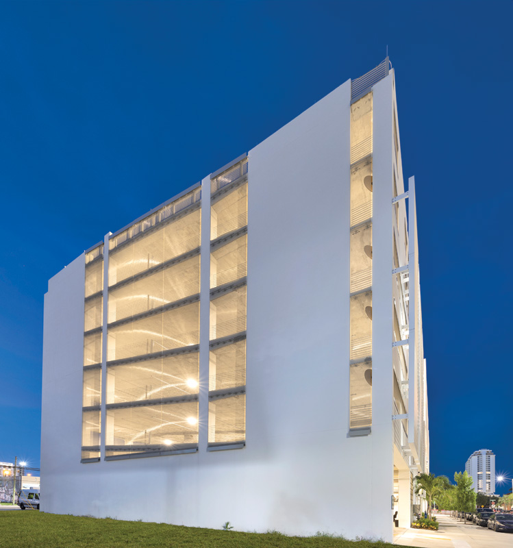 A modern multi-story parking garage illuminated at dusk, showcasing its minimalist white facade and open design.