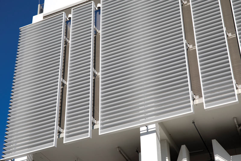 Close-up of modern architectural sunshade slats on a building, showcasing sleek, horizontal lines against a clear blue sky.