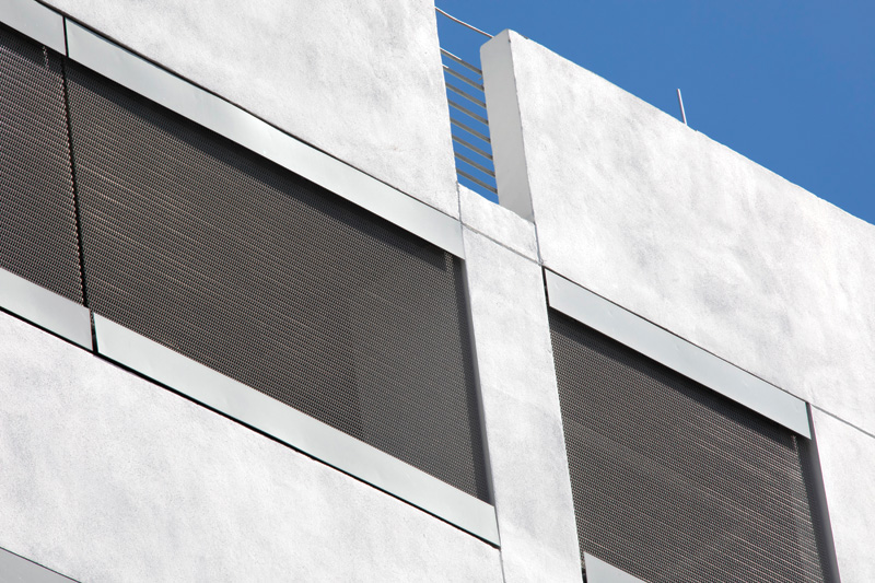 Modern building facade featuring large, mesh-covered windows and sleek metallic trim against a clear blue sky.