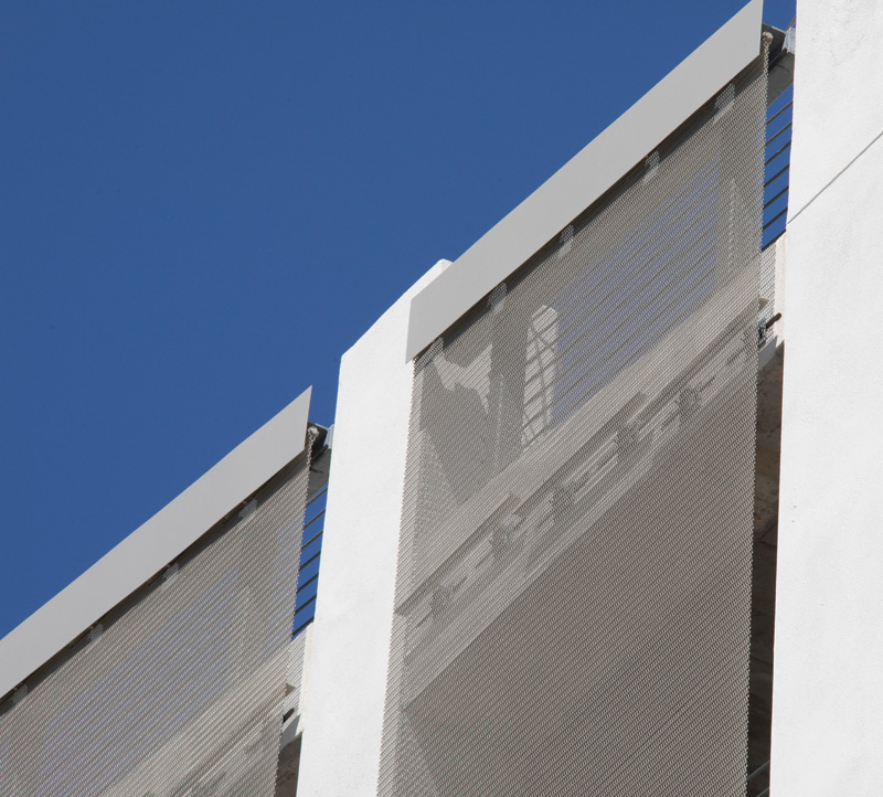 Close-up of a modern building facade featuring a mesh screen against a clear blue sky.