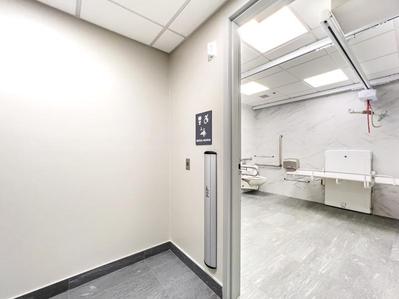 Interior view of a clean, well-lit accessible restroom with signage and safety features, featuring grab bars and a spacious layout.