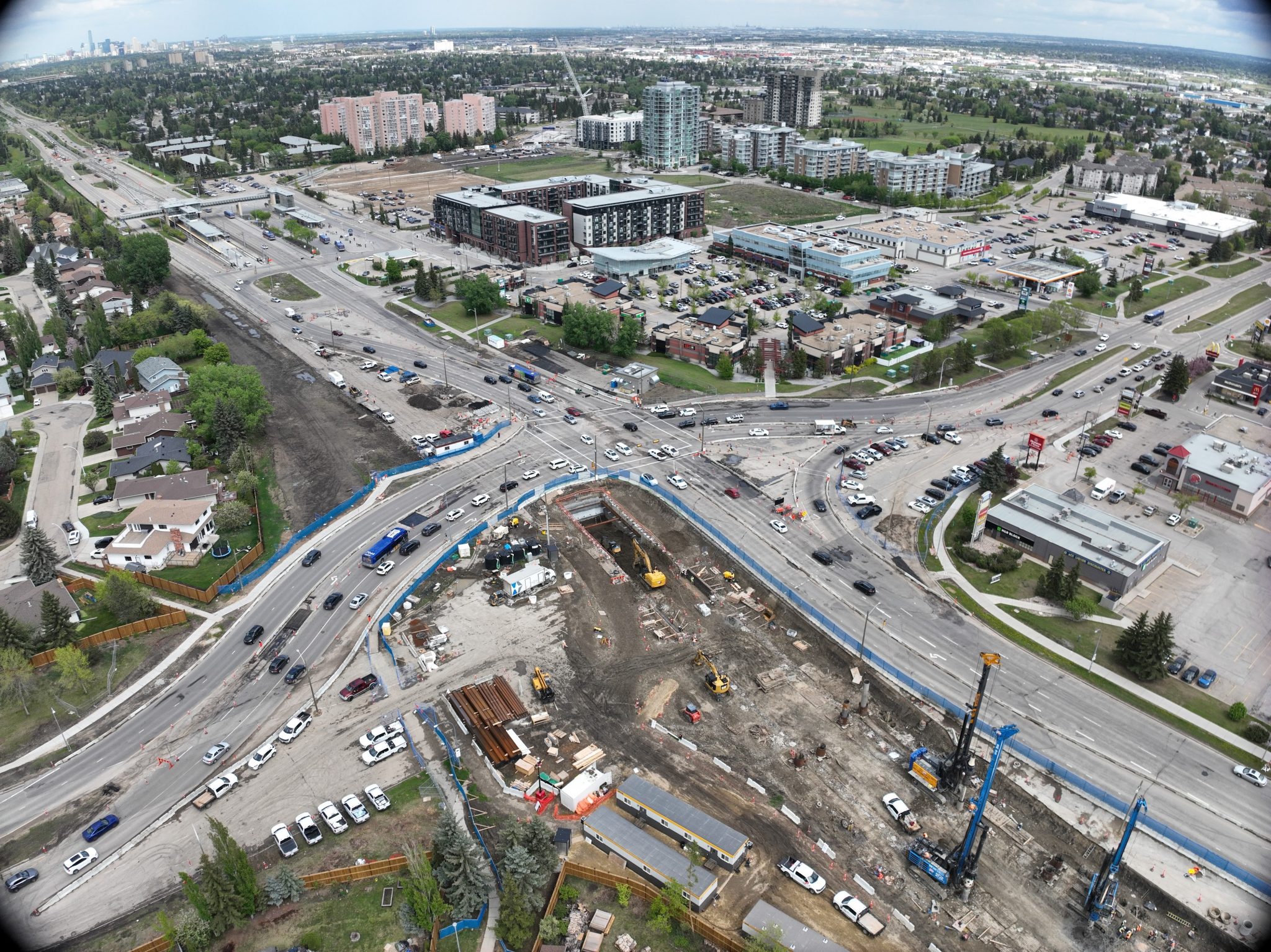 Aerial view of a busy intersection under construction, surrounded by residential and commercial buildings with cars in traffic.