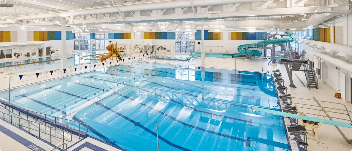 A spacious indoor swimming pool with clear water, diving boards, a water slide, and colorful wall decorations.
