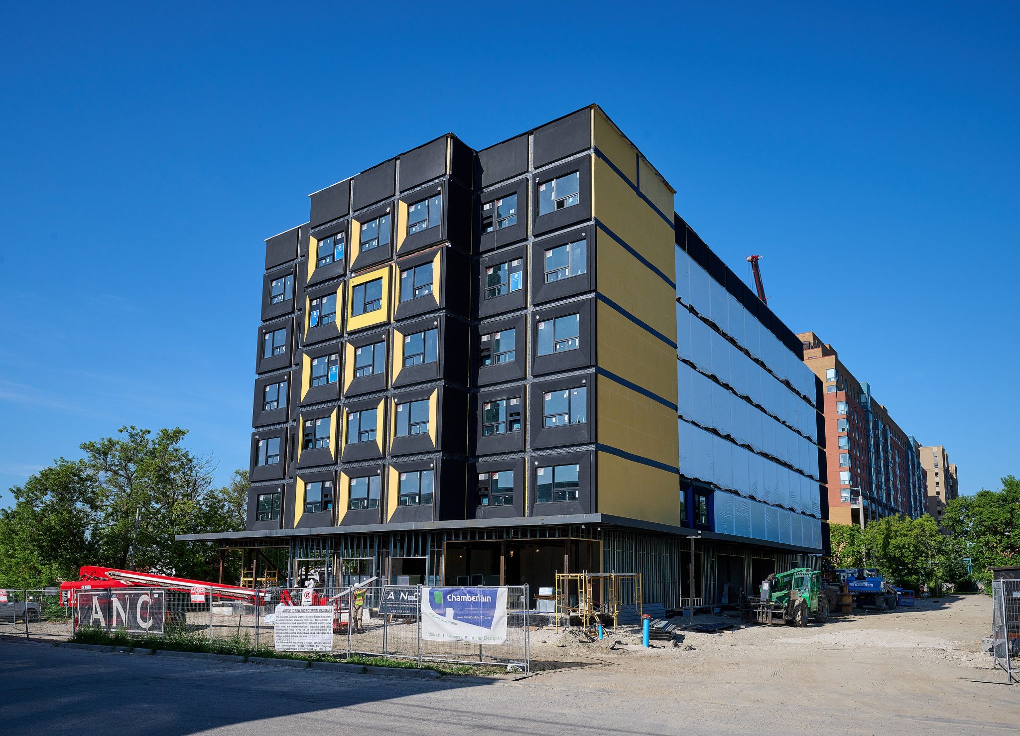 Newly constructed multi-story building featuring black and yellow panels, surrounded by construction equipment and a clear blue sky.