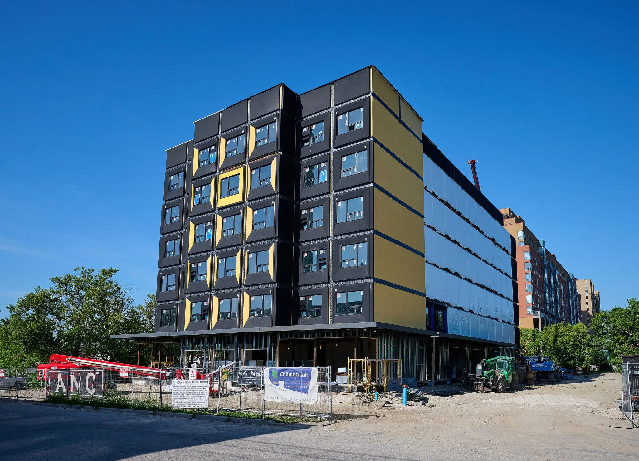 Newly constructed multi-story building featuring black and yellow panels, surrounded by construction equipment and a clear blue sky.