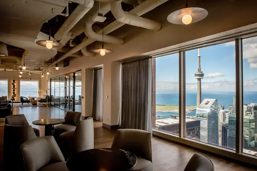 Modern lounge with a view of Toronto's skyline, featuring the CN Tower and a bright, airy atmosphere with stylish seating.