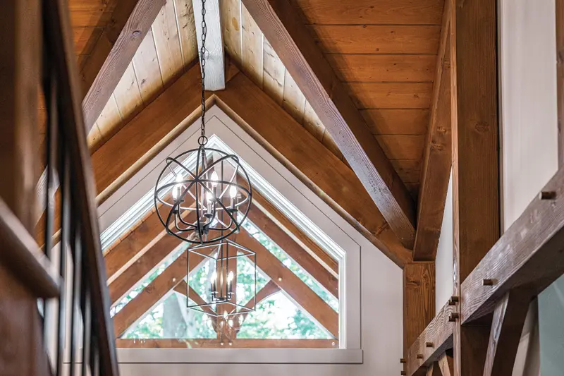 Wooden vaulted ceiling with exposed beams, featuring an elegant geometric chandelier and large triangular windows.