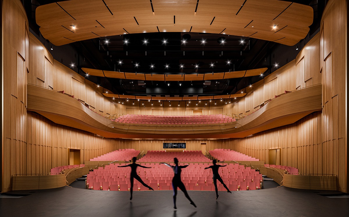 A modern theater interior with wooden walls, pink seats, and stage silhouettes of dancers, showcasing an elegant design and spacious layout.