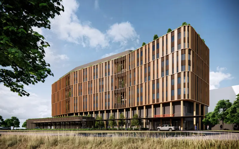 A modern multi-story building with wood-paneled exterior, featuring greenery on rooftops, an emergency entrance, and surrounding landscaping.