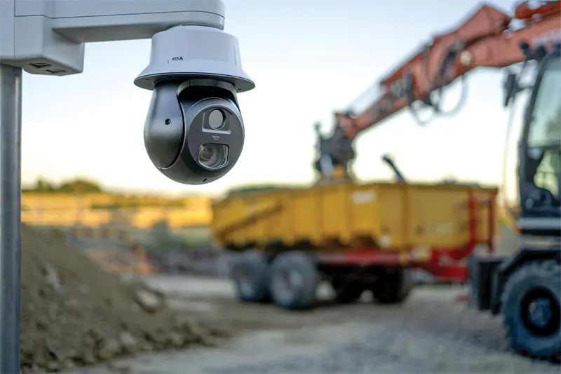 Surveillance camera overlooking an active construction site with a yellow dump truck and excavator in the background.