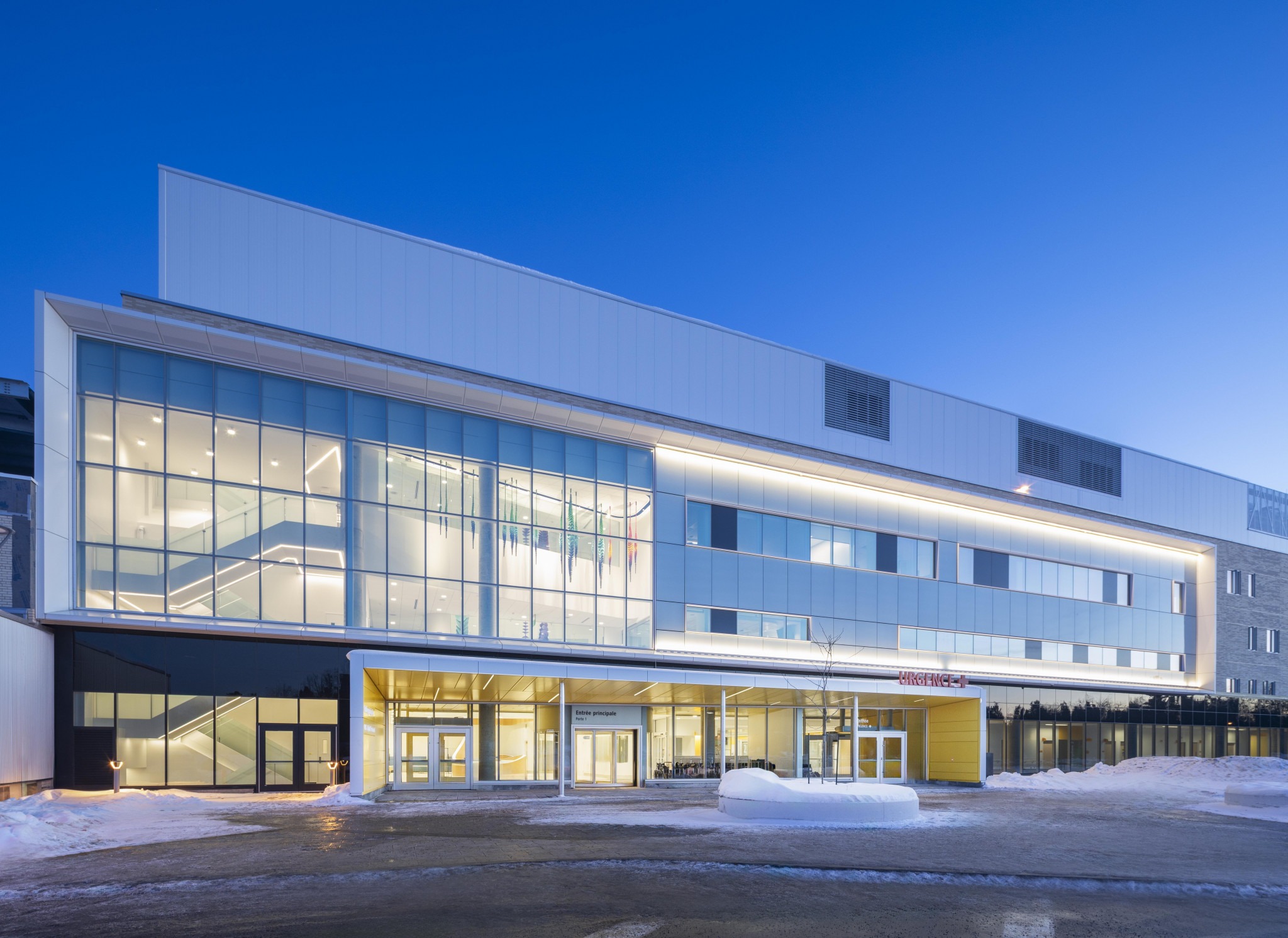 Modern hospital building entrance at dusk with large glass windows.