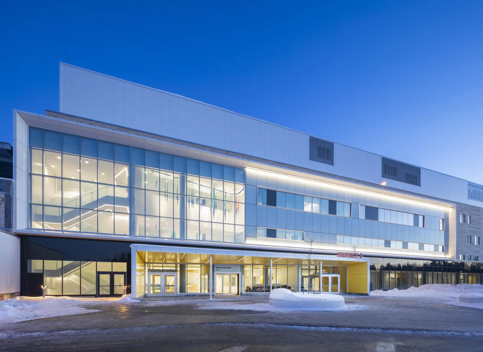 Modern hospital building entrance at dusk with large glass windows.