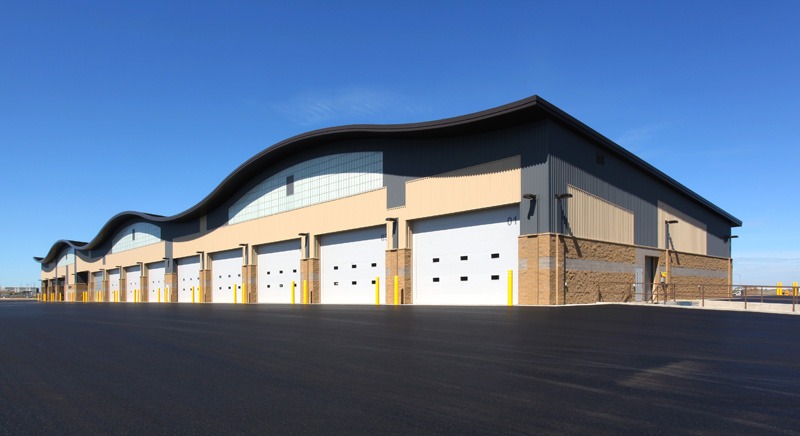 Industrial building with wavy roofline, large white garage doors, and brick base. Clear sky enhances the modern, spacious design.