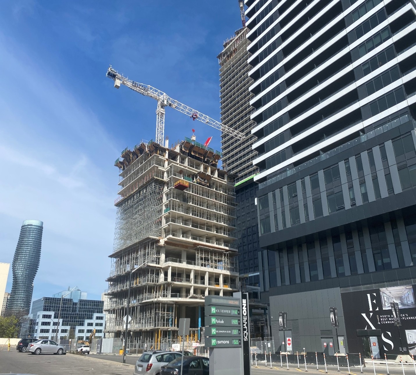 A construction site with a high-rise building under development, surrounded by cranes and modern skyscrapers against a clear blue sky, suggesting urban growth.
