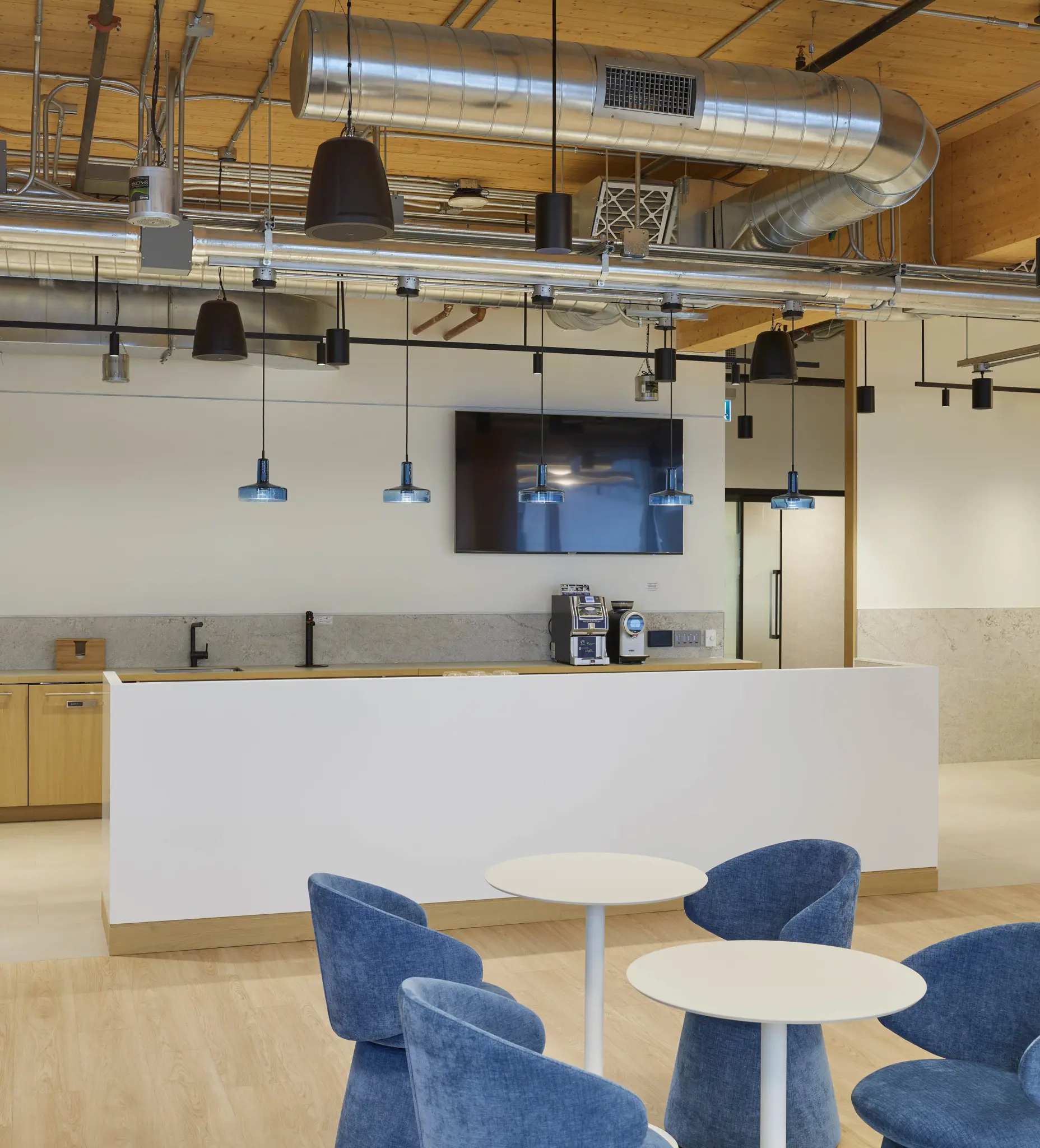 Modern office with open workstations and glass-walled meeting booths. Natural light, wooden accents, and carpeted floors create a calm, professional atmosphere.