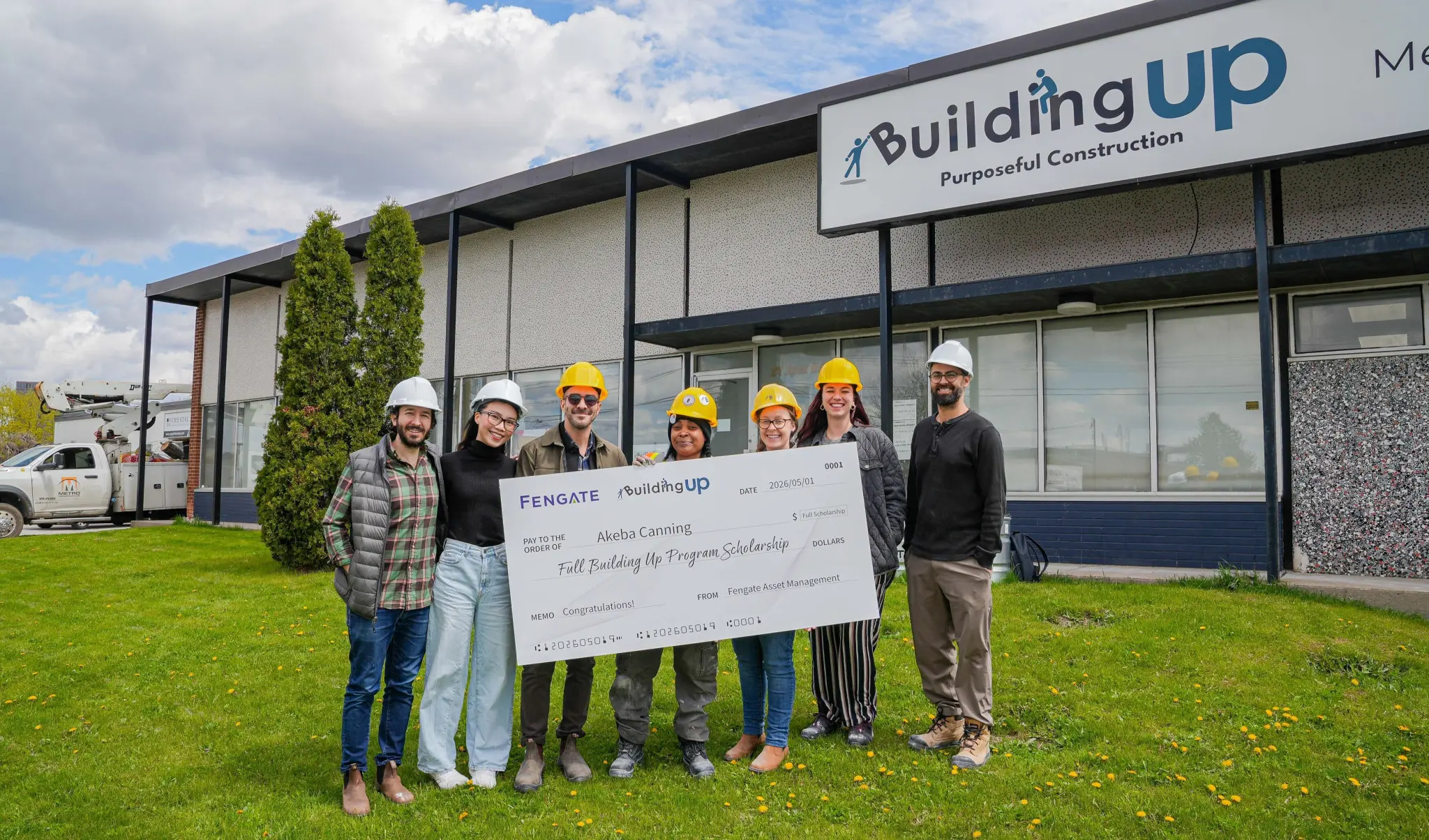 A group of seven people wearing hard hats stand smiling in front of a building labeled 