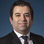 A man in a suit and tie smiles confidently, showcasing a professional appearance and positive demeanor.
