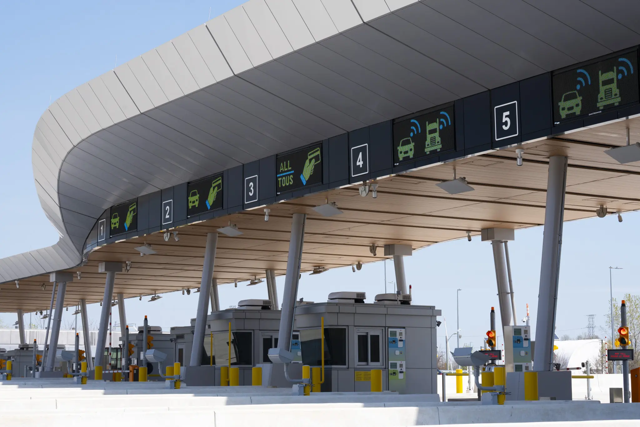 A modern toll plaza with a curved roof, digital displays for vehicle types and payment options, and multiple toll lanes.