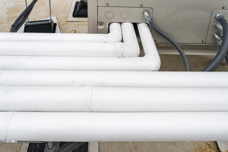 White insulated pipes connected to HVAC equipment on a concrete surface, with gray cables. The setup conveys functionality and industrial efficiency.