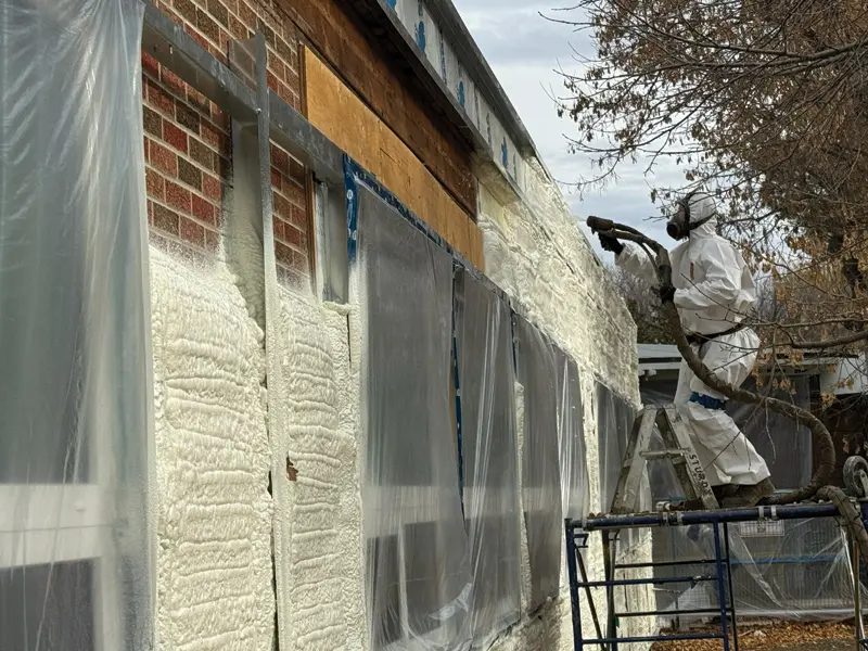 A man in a white protective suit sprays a building with a chemical solution, ensuring safety and cleanliness.