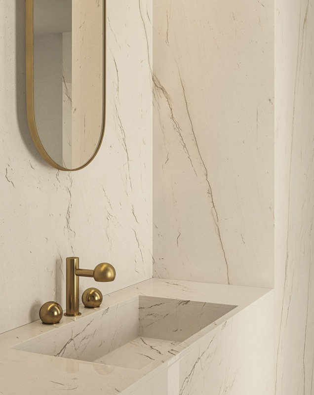 Elegant bathroom with a marble vanity, gold faucet, and oval mirror on a textured beige wall. The space feels minimalist and luxurious.