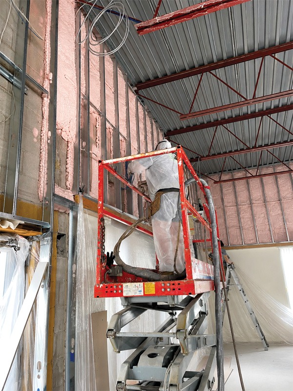 A worker in protective gear is using a scissor lift to install insulation on an interior wall in a construction site.