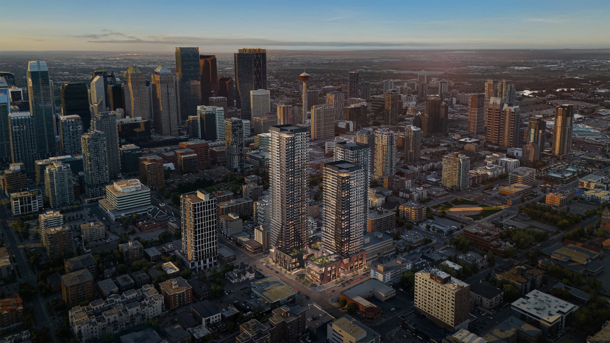 Aerial view of a city skyline at dusk, featuring modern skyscrapers, two prominent residential towers with green spaces, and the Calgary Tower in the center against a pastel sky.