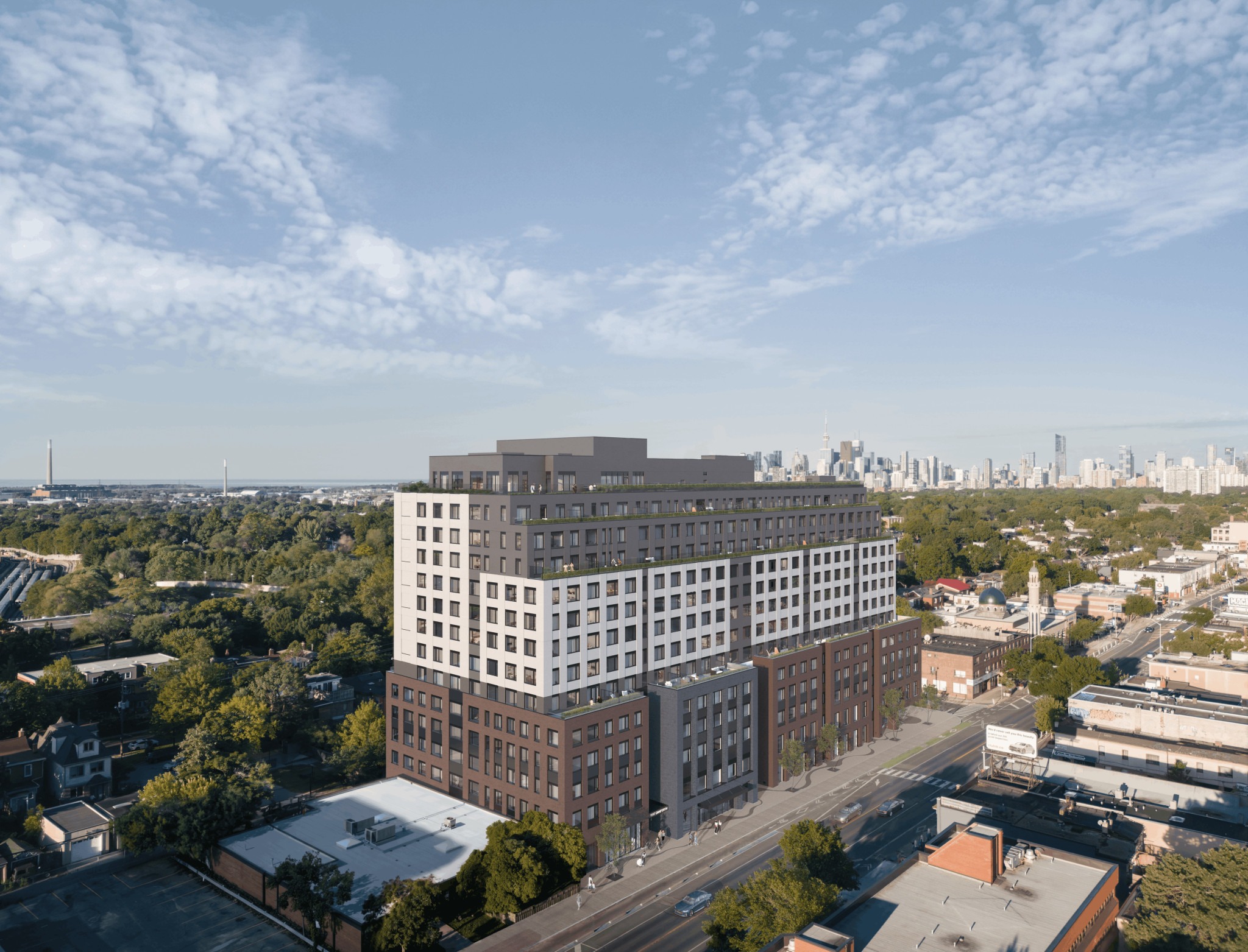 A multi-story modern building with a two-tone facade, surrounded by greenery and smaller structures, with a city skyline visible in the background under a bright, cloudy sky.